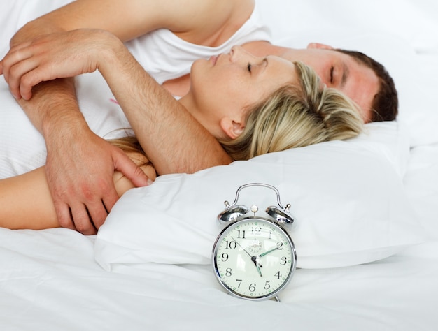 Pareja en la cama con enfoque en reloj despertador