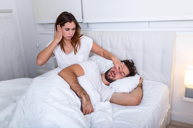 Foto pareja en la cama, el hombre ronca y la mujer no puede dormir. hombre y mujer joven que ronca. pareja durmiendo en la cama. la niña no puede dormir debido a los ronquidos de su hombre tapándose la nariz. problema del hombre que ronca