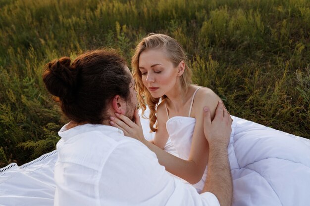 Una pareja en la cama en el verano al atardecer abraza.