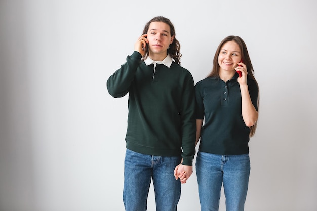 Foto pareja en camisas verdes con teléfonos en las manos sobre fondo blanco hombre y mujer joven usando teléfonos