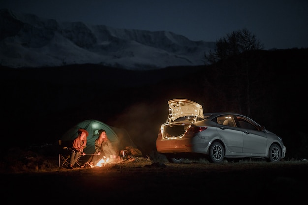 Pareja en camping con fogata en la noche en las montañas