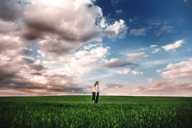 Pareja entre el campo verde y el hermoso cielo. Pareja caminando al aire libre tomados de la mano sonriendo