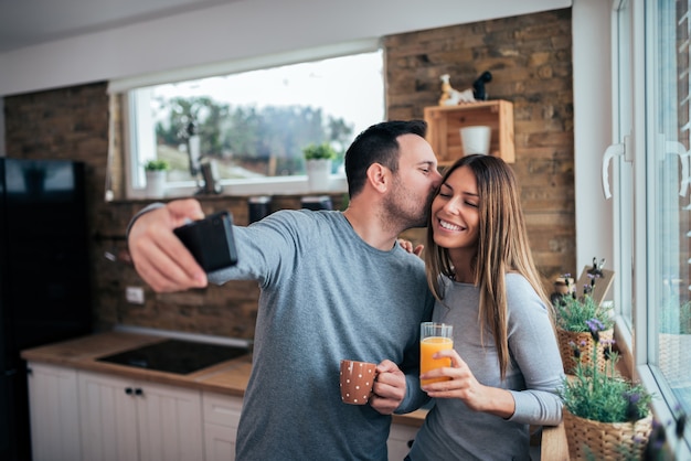 Pareja cariñosa haciendo selfie en la mañana. beber zumo de naranja y café en la cocina.