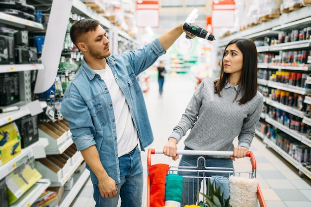 Pareja con carro en el mercado, departamento de herramientas eléctricas, compras familiares. Clientes en la tienda, compradores que eligen bienes de consumo.