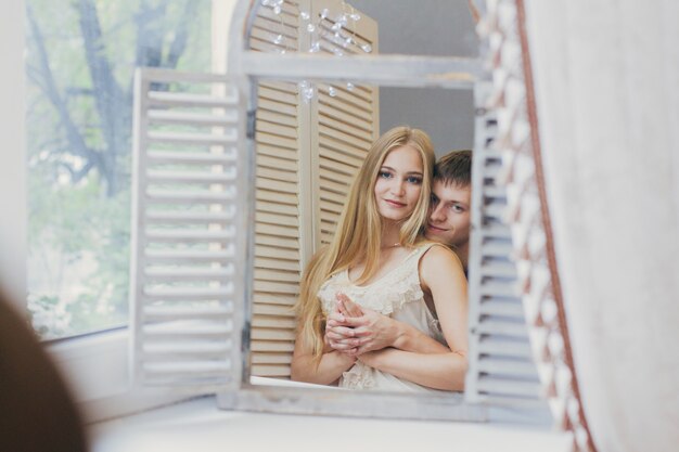 Pareja en casa mirando en el espejo cerca de la ventana