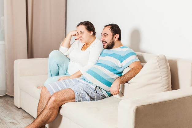 Pareja en casa relajándose en el sofá. Hombre joven y mujer viendo la televisión.