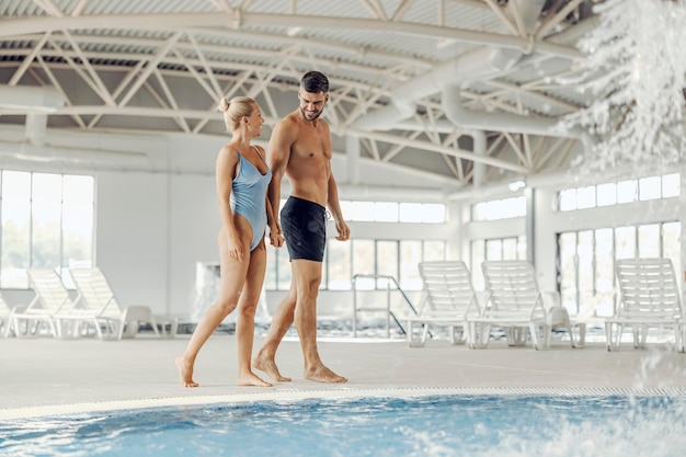 Una pareja casada en traje de baño se toma de la mano y camina junto a una piscina con agua termal