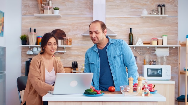 Pareja casada viendo receta en línea mientras prepara ensalada saludable con verduras. Marido y mujer cocinando comida receta. Feliz estilo de vida saludable juntos. Familia en busca de comida en línea. Salud fr