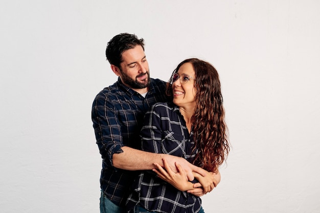 Una pareja caucásica adulta en camisas a cuadros de pie y mostrando los pulgares hacia la cámara y sonriendo sobre un fondo blanco.