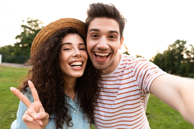 Pareja caucásica caminando en el parque verde y tomando selfie en smartphone