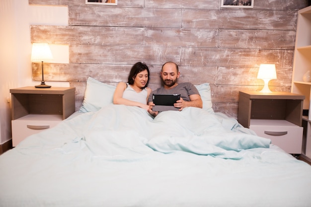 Pareja caucásica casada en pijama con tablet PC antes de dormir.