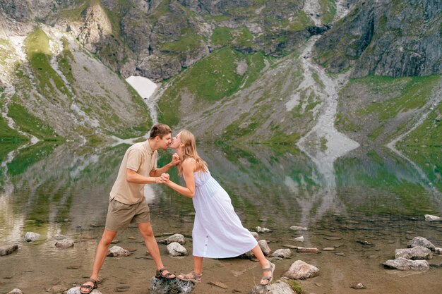 Pareja caucásica divirtiéndose en frente del lago de montaña con reflejos.