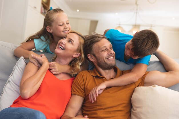 Pareja caucásica con hija e hijo sentados en el sofá y sonriendo en casa. familia disfrutando de tiempo libre de calidad juntos.