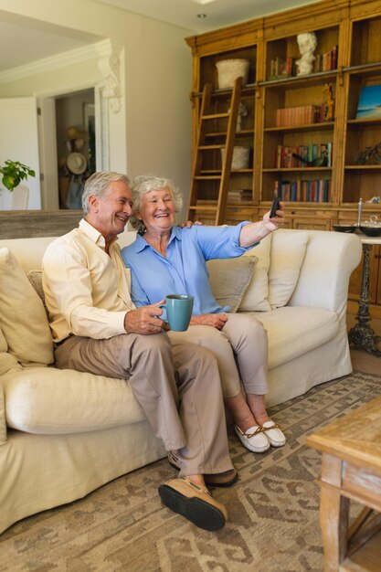 Una pareja caucásica mayor sentada en un sofá haciendo videollamadas usando un teléfono inteligente. concepto de retiro, jubilación y estilo de vida feliz para personas mayores.