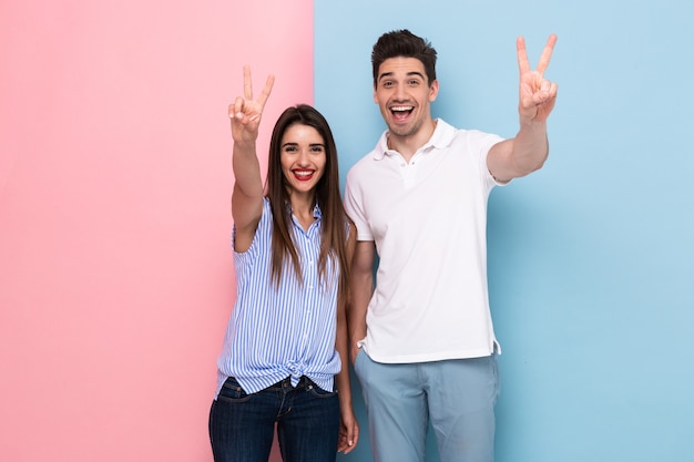 Pareja caucásica en ropa casual sonriendo y gesticulando el signo de la paz, aislado sobre pared colorida