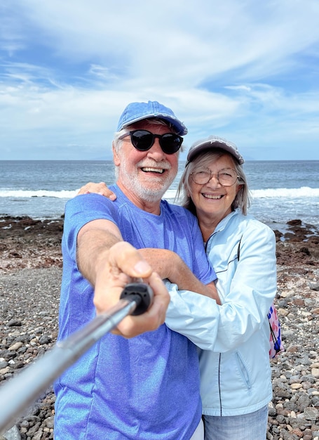 Una pareja caucásica senior despreocupada abrazándose de pie al aire libre juntos en la playa tomando fotos