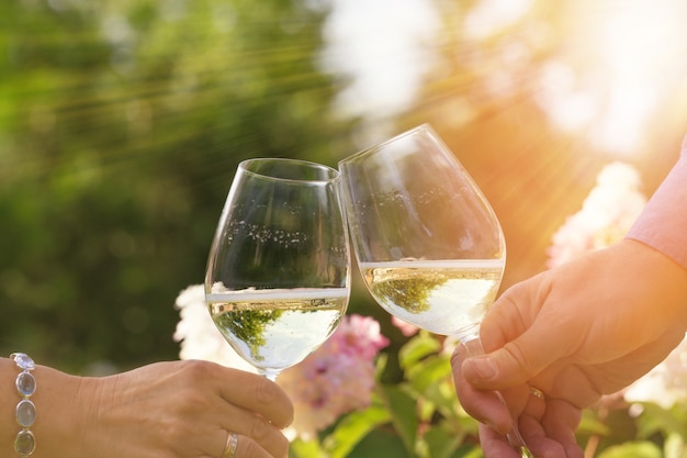 Pareja celebra románticamente al aire libre con vasos de vino blanco, proclama brindis Gente cenando en el jardín de una casa en la luz del sol del verano.