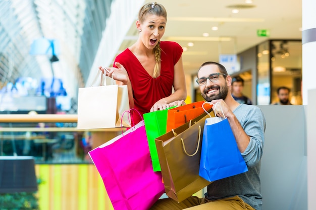 Foto pareja en centro comercial con bolsas sentadas para descansar