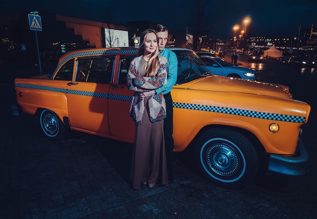 Foto pareja cerca de un taxi amarillo en la noche en la calle de la ciudad