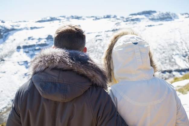 Foto pareja en chaquetas mirando montañas nevadas