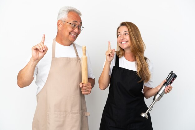 Pareja de chefs de mediana edad aislado sobre fondo blanco con la intención de darse cuenta de la solución mientras levanta un dedo hacia arriba