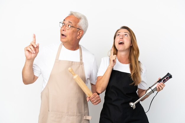 Pareja de chefs de mediana edad aislado sobre fondo blanco pensando en una idea apuntando con el dedo hacia arriba