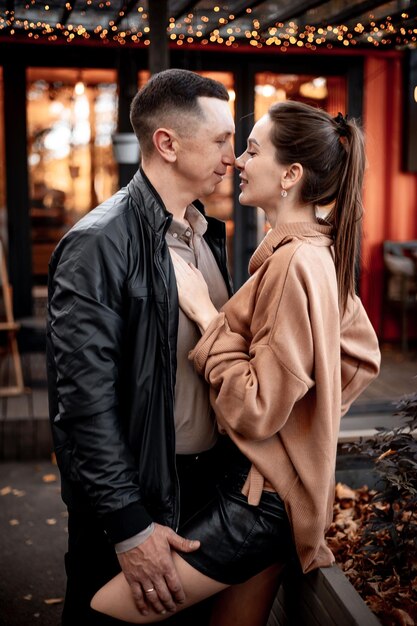 una pareja de chicos jóvenes con una chica en otoño en un café en tonos marrones y naranjas en una terraza al aire libre abrazándose y besándose amor o día de San Valentín