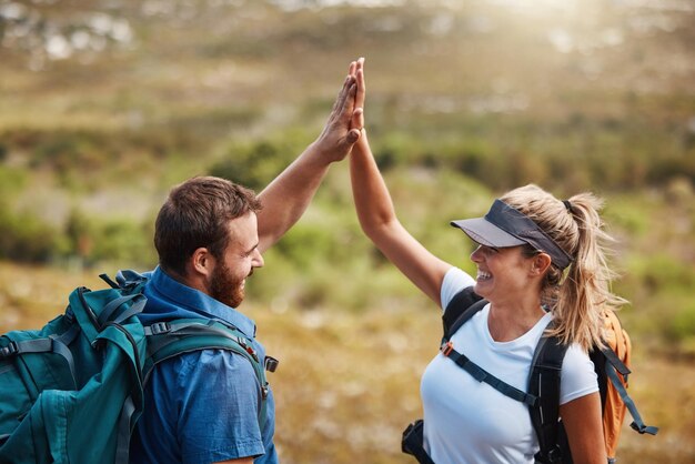 Pareja choca los cinco y camina con el objetivo de motivación y celebración del objetivo de fitness en la naturaleza con mochila Hombre mujer y feliz por la asociación emocionada o apoyada mientras caminan juntos al aire libre