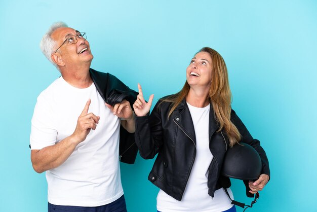 Pareja de ciclistas de mediana edad con un casco de motocicleta aislado sobre fondo azul apuntando con el dedo índice una gran idea