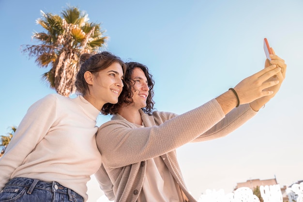 Pareja bajo un cielo azul haciendo selfie con teléfono móvil