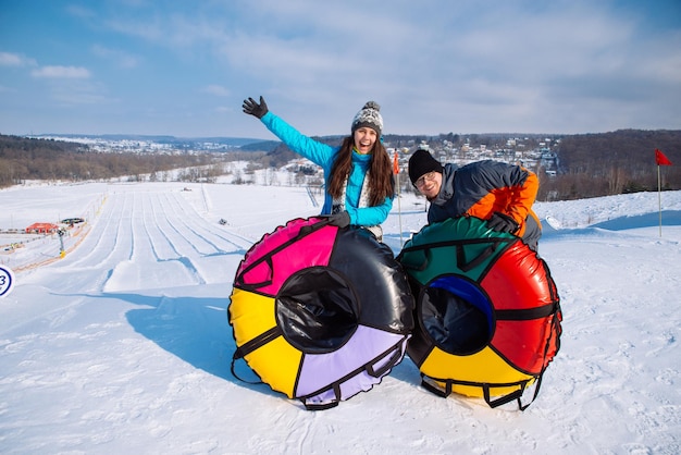 Pareja en la cima de la colina lista para deslizarse desde la parte superior de la actividad invernal de snow tubing