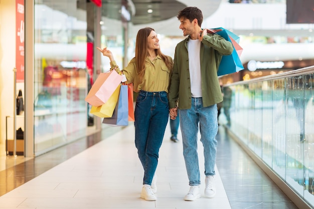 Pareja de clientes comprando caminando llevando bolsas de compras en un centro comercial moderno