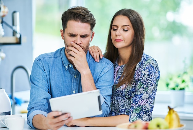 Pareja en la cocina de casa con tableta electrónica