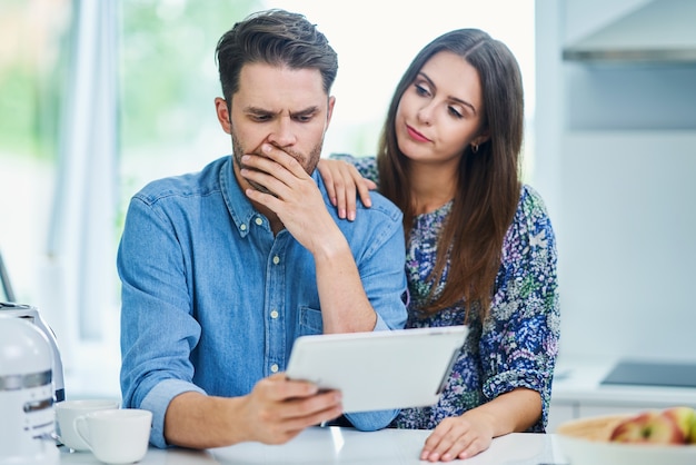 Pareja en la cocina de casa con tableta electrónica