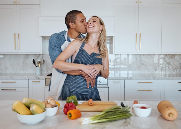 Pareja cocinando comida y amor por las verduras con un beso en la mejilla mientras ayuda con la cena en casa Hombre y mujer en el Reino Unido con una dieta de estilo de vida saludable y alimentación vegana para la salud y el bienestar