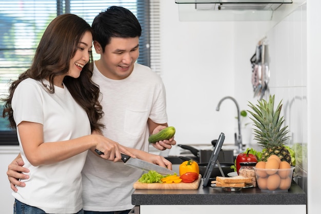 Foto pareja cocinando y preparando verduras según una receta en una tableta en la cocina de casa