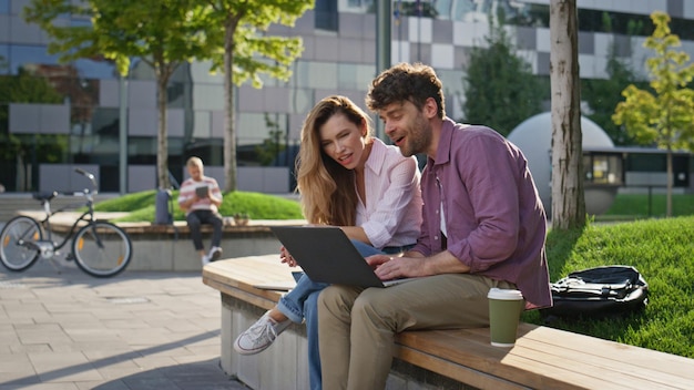 Una pareja de colegas mirando una computadora portátil en un parque soleado sonriendo socios trabajando afuera