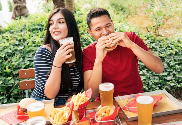 Pareja comiendo comida rápida en la mesa con cerveza