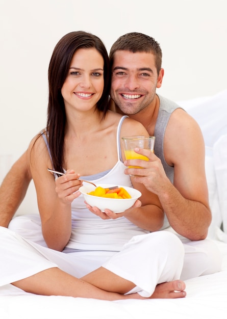 Pareja comiendo fruta y jugo de naranja en la cama