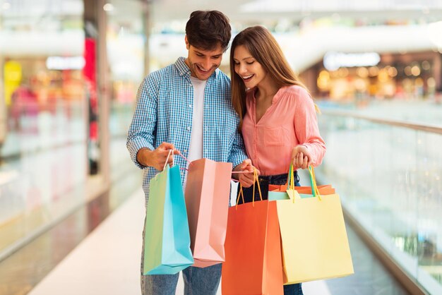 Pareja de compradores felices mirando bolsas de compras en el hipermercado