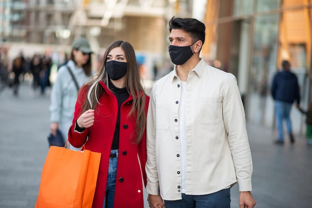 Pareja de compras de covid y coronavirus caminando en una ciudad mientras lleva bolsas de compras