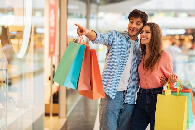 Pareja de compras juntos esposo señalando con el dedo a la tienda en el centro comercial