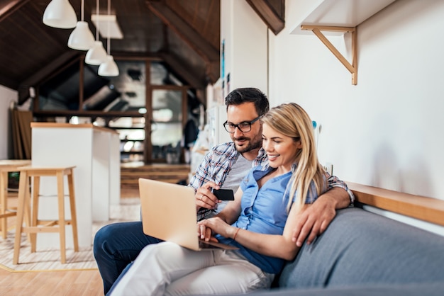 Pareja de compras en línea mientras está sentado en el sofá en el apartamento moderno.