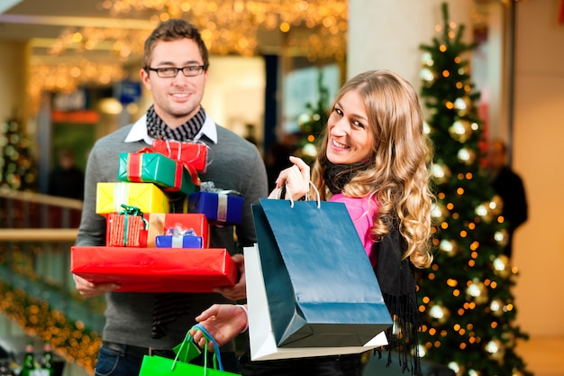 Pareja de compras navideñas con regalos en el centro comercial