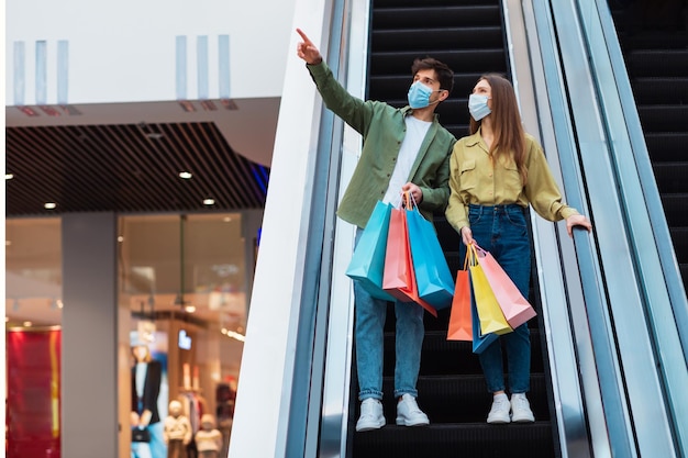 Pareja de compras señalando con el dedo a un lado en un hipermercado con máscaras faciales