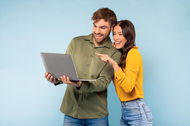 Pareja con computadora portátil sonriendo y apuntando a la pantalla con fondo azul