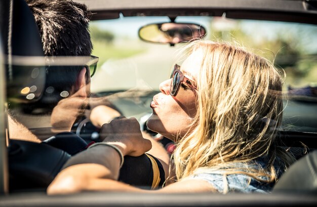 Pareja conduciendo un auto convertible y divirtiéndose