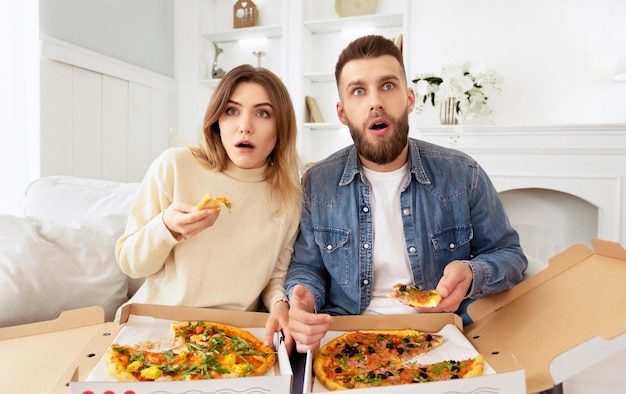Una pareja conmocionada viendo una película y comiendo pizza en casa.