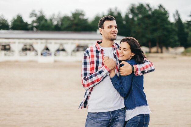 Una pareja contenta envuelta en los brazos de la otra en una playa con la mujer apoyando la cabeza en el pecho del hombre sintiéndose segura y amada