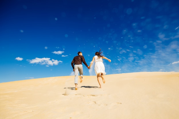 Foto pareja corriendo por la arena y tomados de la mano